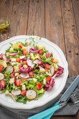 Fresh salad with mixed greens radish cheese and tomato in a plate on wooden background. Italian Mediterranean or Greek cuisine. Vegetarian vegan food.