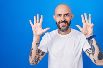 Hispanic man with tattoos standing over blue background showing and pointing up with fingers number...