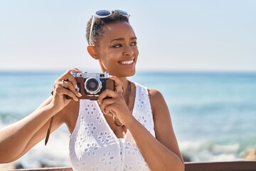 African american woman tourist using vintage camera at seaside