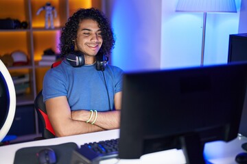 Fototapeta na wymiar Young latin man streamer smiling confident sitting with arms crossed gesture at gaming room