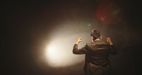 Rear view of male music conductor holding baton against black background - obrazy, fototapety, plakaty