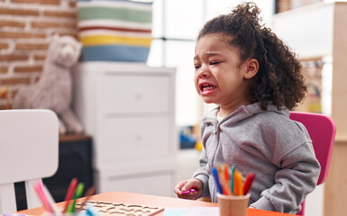 African american toddler sitting on table crying at kindergarten