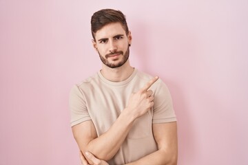 Hispanic man with beard standing over pink background pointing with hand finger to the side showing advertisement, serious and calm face