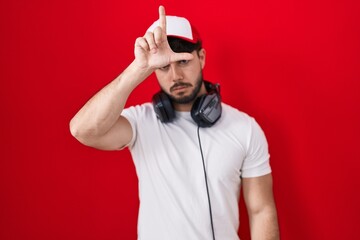 Hispanic man with beard wearing gamer hat and headphones making fun of people with fingers on...