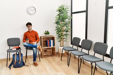 Young hispanic man smiling confident drinking coffee at waiting room