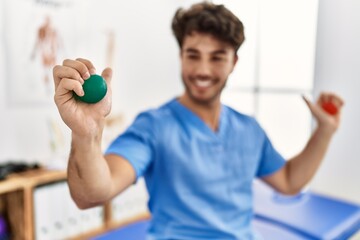 Young hispanic man wearing physio therapist uniform using anti stress ball at clinic