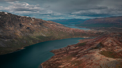 Blue lake in mountain landscape from above the hike to Knutshoe summit in Jotunheimen National Park in Norway, mountains of Besseggen in background, cloudy sky