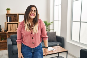 Young hispanic woman working at the office wearing glasses with a happy and cool smile on face....