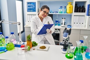 Young beautiful plus size woman scientist smiling confident writing report working at pharmacy