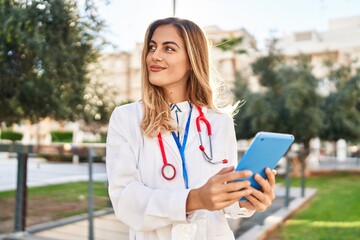 Young blonde woman wearing doctor uniform using touchpad at park