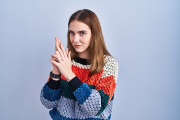 Young hispanic girl standing over blue background holding symbolic gun with hand gesture, playing killing shooting weapons, angry face