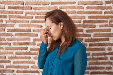 Brunette woman standing over bricks wall tired rubbing nose and eyes feeling fatigue and headache. stress and frustration concept.