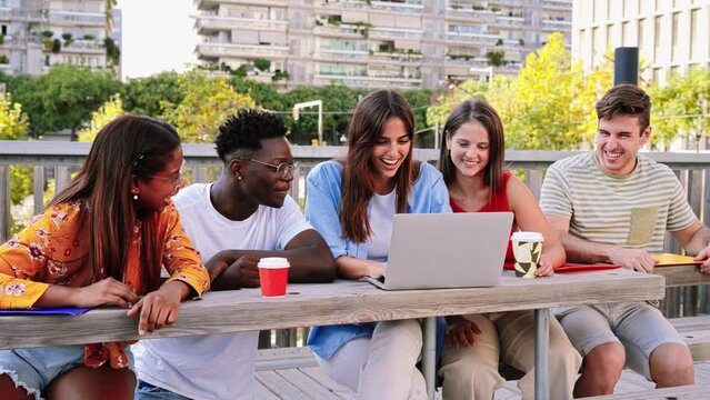A group of five multicultural teenage students searching information on a laptop in the university campus. Happy college young people smiling doing homeworks and studying on a computer. Slow motion