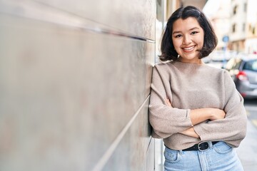 Young woman standing with arms crossed gesture looking to the camera at street