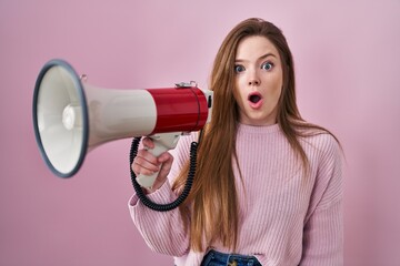 Young caucasian woman shouting through megaphone scared and amazed with open mouth for surprise, disbelief face