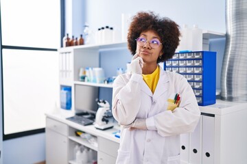 Young african american woman working at scientist laboratory thinking concentrated about doubt with finger on chin and looking up wondering