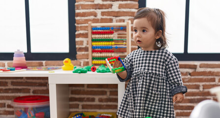 Adorable chinese girl holding toy standing with relaxed expression at kindergarten