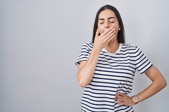 Young brunette woman wearing striped t shirt bored yawning tired covering mouth with hand. restless and sleepiness.