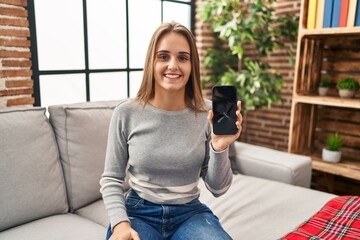Young woman holding broken smartphone showing cracked screen looking positive and happy standing and smiling with a confident smile showing teeth
