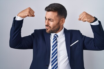 Handsome hispanic man wearing suit and tie showing arms muscles smiling proud. fitness concept.