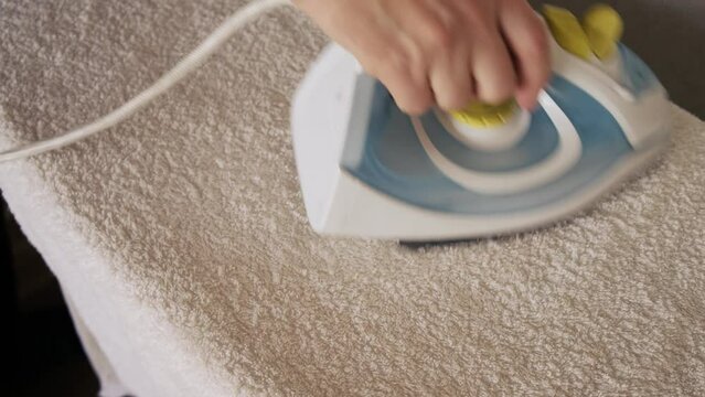 A man's hand with an iron is ironing a terry towel. Close-up