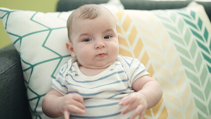 Adorable caucasian baby sitting on sofa with relaxed expression at home