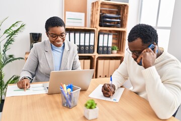 Man and woman business workers using laptop and talking on the smartphone at office