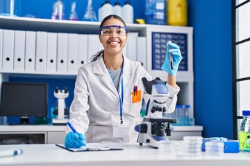 Young african american woman scientist analysing blood test tube writing report at laboratory