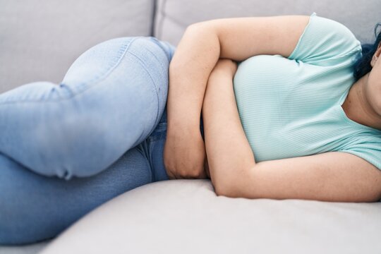 Young caucasian woman suffering for menstrual pain lying on sofa at home