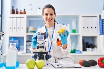 Young beautiful hispanic woman scientist using microscope holding lemon at laboratory