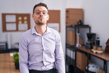 Fototapeta premium Young hispanic man at the office looking at the camera blowing a kiss on air being lovely and sexy. love expression.