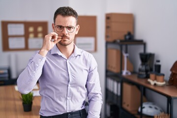 Young hispanic man at the office mouth and lips shut as zip with fingers. secret and silent, taboo...
