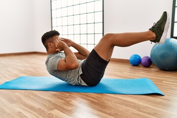 Young hispanic man training abs exercise at sport center