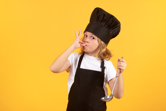 Funny Kid Chef Cook With Kitchen Ladle, Studio Portrait. Kid In Cooker Uniform And Chef Hat Preparing Food On Studio Color Background. Cooking, Culinary And Kids Food Concept.