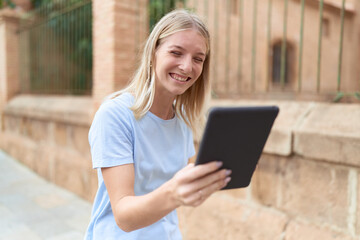 Fototapeta premium Young blonde woman smiling confident using touchpad at street