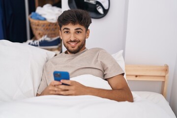 Young arab man using smartphone sitting on bed at bedroom