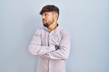 Arab man with beard standing over blue background looking to the side with arms crossed convinced and confident