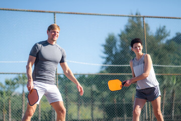 couple playing pickleball game, hitting pickleball yellow ball with paddle, outdoor sport leisure...