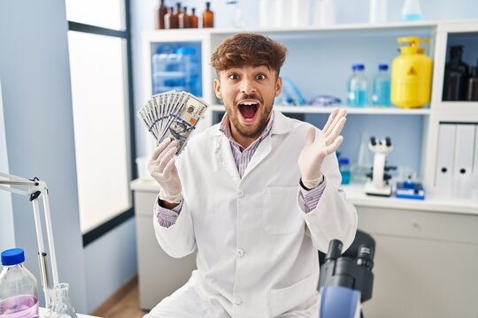 Arab man with beard working at scientist laboratory holding money celebrating victory with happy smile and winner expression with raised hands