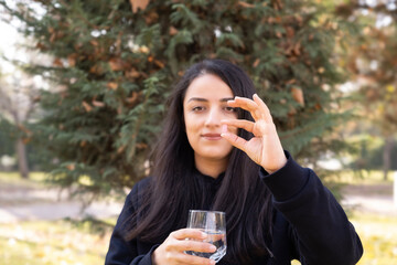 Holding pill, beautiful millennial smiling woman holding pill. Glass of water on her hand. Presenting new effective vitamin medicine supplement. Selective focus on hand. Copy space. Pharmacy concept.