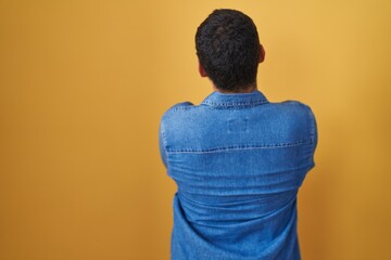 Hispanic man standing over yellow background standing backwards looking away with crossed arms