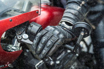 Hand in safety glove on red motorcycle handlebar during snowfall