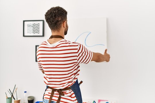Young arab artist man on back view hanging draw canvas on wall at art studio.