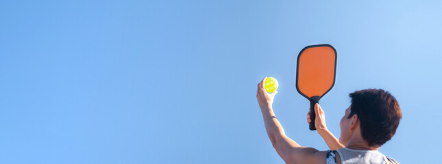 Pickleball banner over blue sky, woman playing pickleball game, hitting pickleball yellow ball with paddle, outdoor sport leisure activity, copyspace for text.