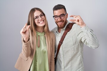 Young couple standing over white background smiling and confident gesturing with hand doing small size sign with fingers looking and the camera. measure concept.