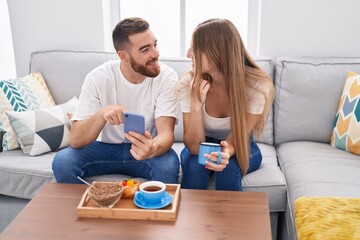 Man and woman couple having breakfast using smartphone at home