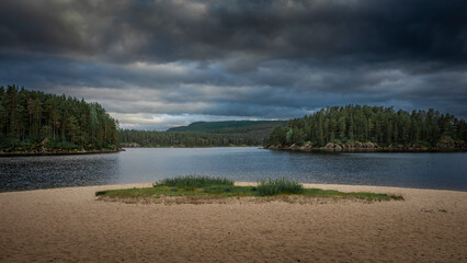 Sand beach with trees on lake in Sorlandet Norway under dramatic cloudy sky