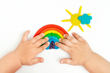 Baby hands making rainbow, cloud, sun with rays from modeling clay. Toddler development.
