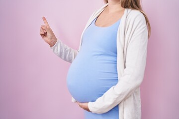 Young pregnant woman expecting a baby, touching pregnant belly smiling happy pointing with hand and finger to the side