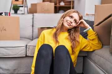 Obraz premium Young blonde woman smiling confident sitting on floor at new home